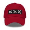A classic XXX Dad Cap in red, showcasing a black rectangular patch with three white embroidered Amsterdam Crosses in a row on the front. A classic XXX Dad Cap in red, showcasing a black rectangular patch with three white embroidered Amsterdam Crosses in a row on the front.