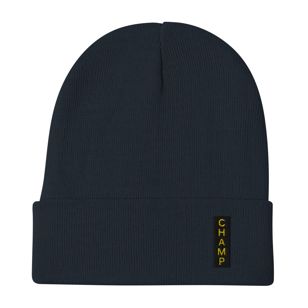 The Subtle & Mighty CHAMP Embroidered Beanie features a dark color, folded brim, and CHAMP in yellow on a vertical patch.