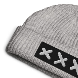 A close-up of the XXX embroidered FISHERMAN Beanie - Bold & Brave in gray, showcasing its bold knit and a black patch with three white stitched Xs in a row on the folded brim.