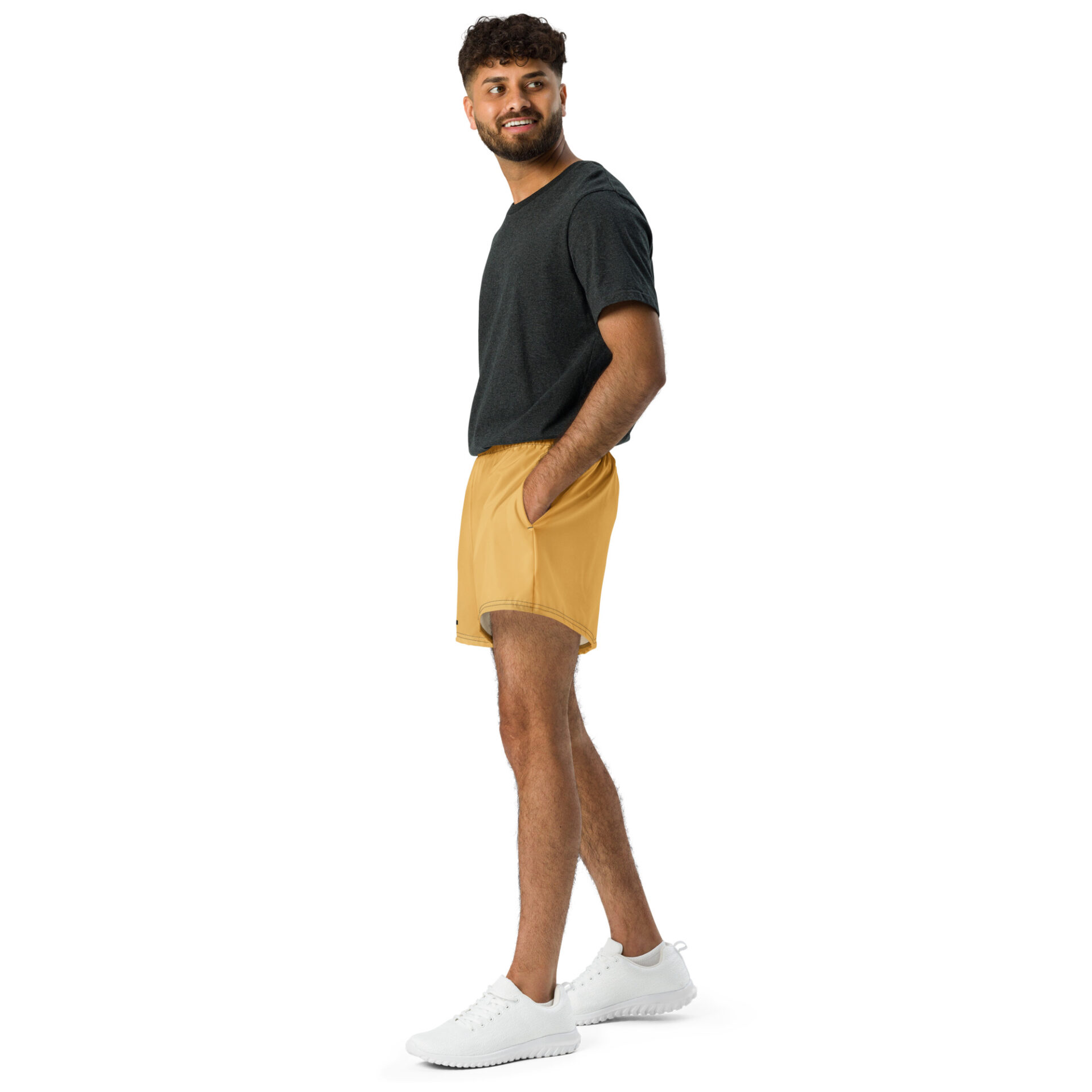Man in a dark gray top, CHAMP Golden Athletic Shorts, and white sneakers stands smiling against a plain white background. Man in a dark gray top, CHAMP Golden Athletic Shorts, and white sneakers stands smiling against a plain white background.