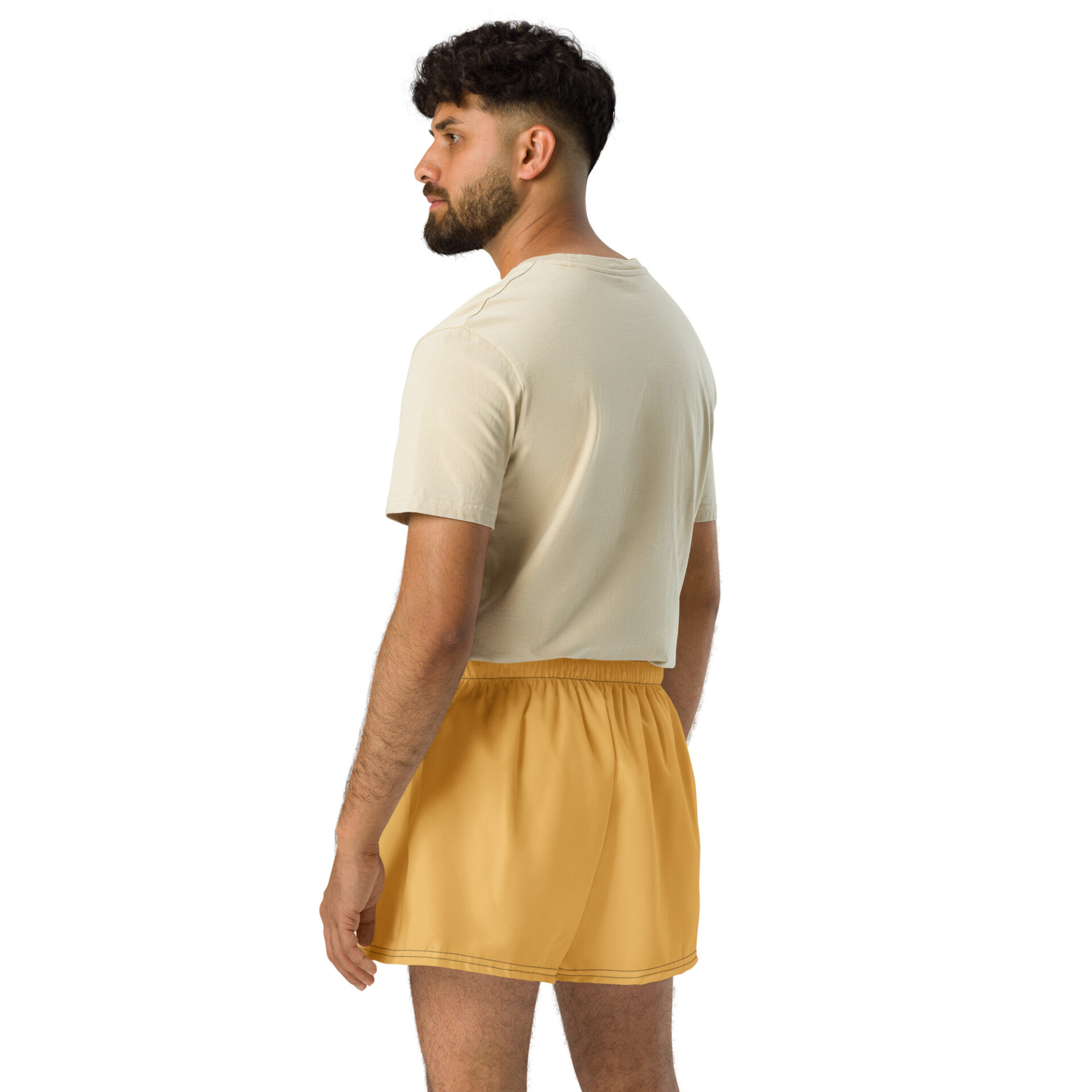 A bearded man in a beige crop top and CHAMP Golden Athletic Shorts stands facing left, gazing sideways. A simple white background accentuates his stylish look. A bearded man in a beige crop top and CHAMP Golden Athletic Shorts stands facing left, gazing sideways. A simple white background accentuates his stylish look.