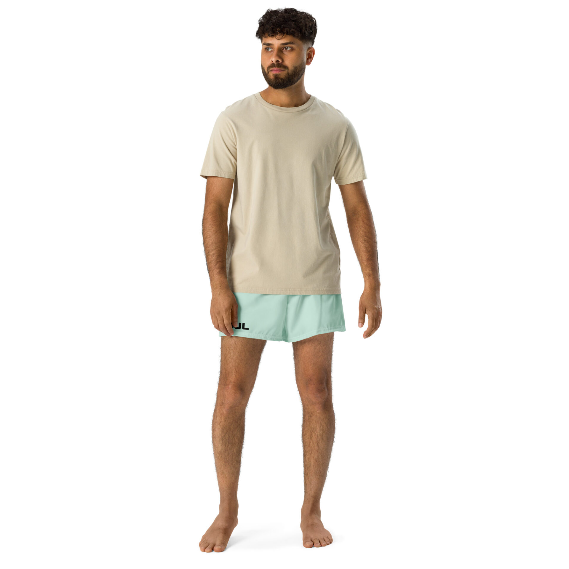 A barefoot man with short curly hair and a beard wears a beige T-shirt and light blue MJL Athletic Shorts featuring a black logo on the left leg, posed against a plain white background. A barefoot man with short curly hair and a beard wears a beige T-shirt and light blue MJL Athletic Shorts featuring a black logo on the left leg, posed against a plain white background.