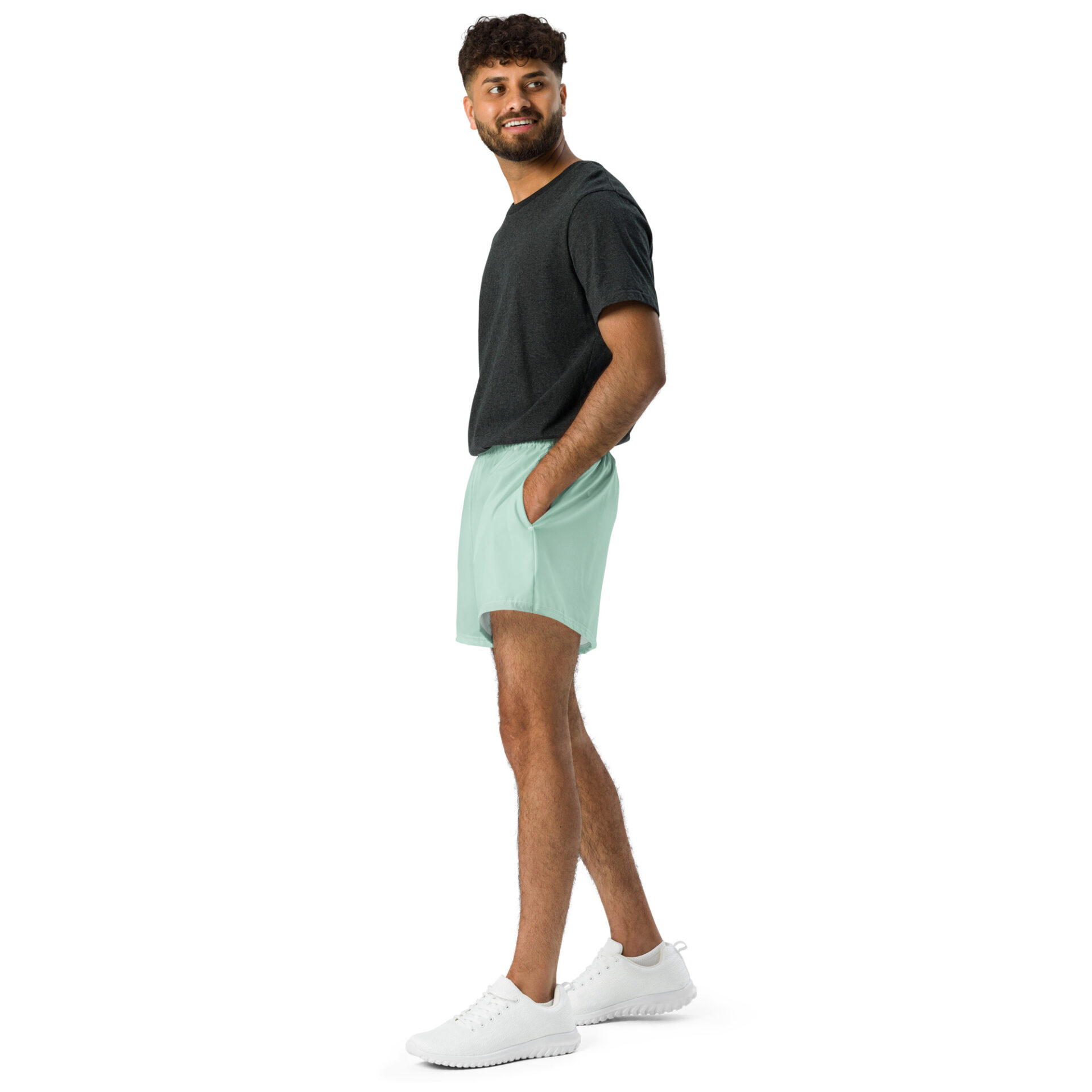 A man stands sideways with one hand in his pocket, wearing a dark t-shirt, MJL Athletic Shorts in light green, and white sneakers, set against a plain white background. A man stands sideways with one hand in his pocket, wearing a dark t-shirt, MJL Athletic Shorts in light green, and white sneakers, set against a plain white background.