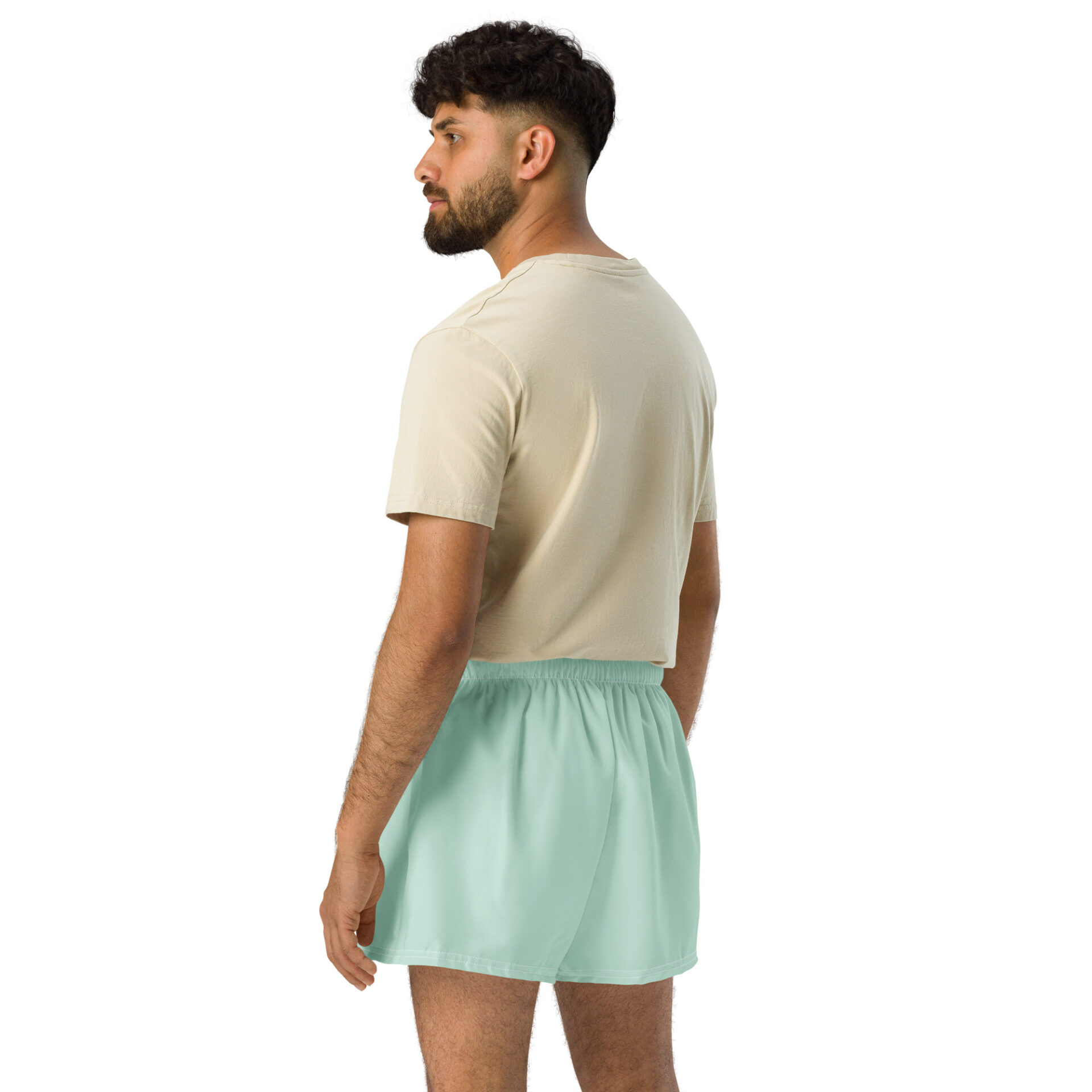 A man with dark hair and a beard wears a beige t-shirt and light green MJL Athletic Shorts, standing turned slightly away against a plain white background. A man with dark hair and a beard wears a beige t-shirt and light green MJL Athletic Shorts, standing turned slightly away against a plain white background.