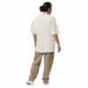 A person with long dark hair in a bun stands facing away, wearing an ADAM XXX TANTOE OUD Oversized faded t-shirt, tan cargo pants, and white shoes against a dark background. A person with long dark hair in a bun stands facing away, wearing an ADAM XXX TANTOE OUD Oversized faded t-shirt, tan cargo pants, and white shoes against a dark background.