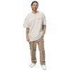 A man with long dark hair tied back is smiling and wearing an ADAM XXX TANTOE OUD Oversized faded t-shirt, khaki cargo pants, and white sneakers, standing with one hand in his pocket against a plain dark background. A man with long dark hair tied back is smiling and wearing an ADAM XXX TANTOE OUD Oversized faded t-shirt, khaki cargo pants, and white sneakers, standing with one hand in his pocket against a plain dark background.
