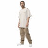 A man with long hair in a ponytail wears an ADAM XXX TANTOE OUD Oversized faded t-shirt, tan cargo pants, and white sneakers, standing against a plain black background. A man with long hair in a ponytail wears an ADAM XXX TANTOE OUD Oversized faded t-shirt, tan cargo pants, and white sneakers, standing against a plain black background.