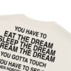 An oversized faded t-shirt in a cream color, featuring bold black text that says: YOU HAVE TO EAT THE DREAM, SLEEP THE DREAM, DREAM THE DREAM, YOU GOTTA TOUCH, YOU HAVE TO SEE IT. An oversized faded t-shirt in a cream color, featuring bold black text that says: YOU HAVE TO EAT THE DREAM, SLEEP THE DREAM, DREAM THE DREAM, YOU GOTTA TOUCH, YOU HAVE TO SEE IT.